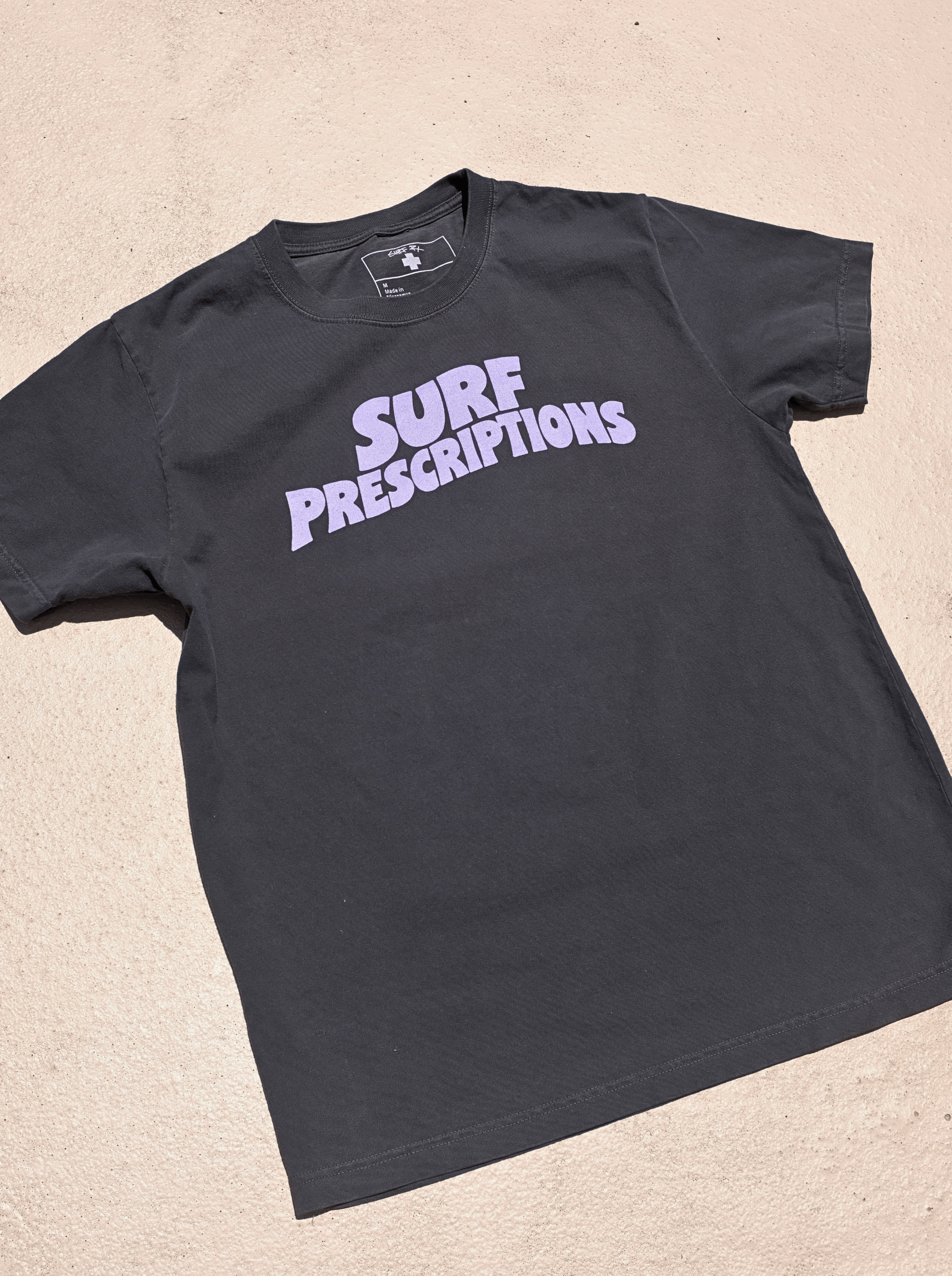 Doom Tee in black with bold purple "Surf Prescriptions" arched lettering across the chest, flat lay